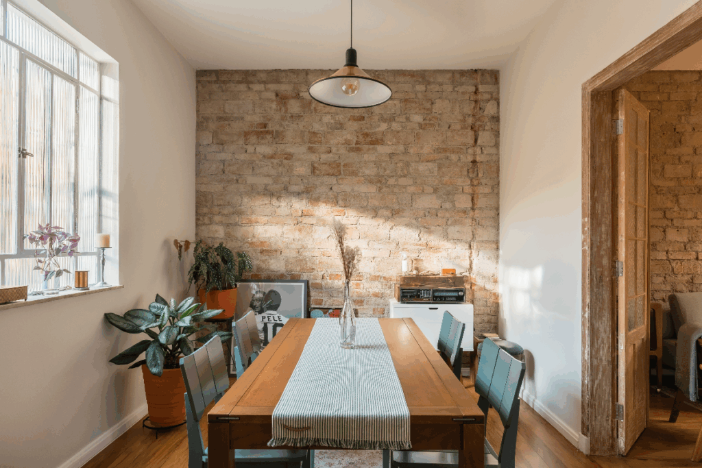 Sala de jantar com parede de tijolinhos, móvel branco, com um quadro de uma imagem e jogadores de futebol com mesa de jantar de madeira com 4 cadeiras  