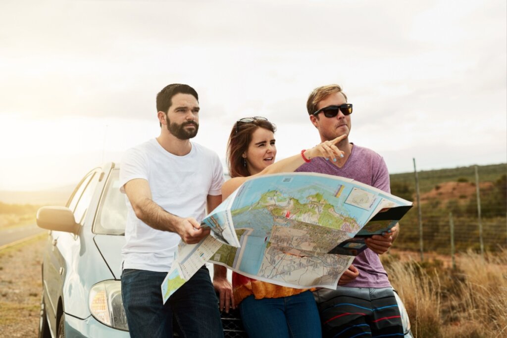 Dois homens e uma mulher sentados no capô do carro e olhando um mapa