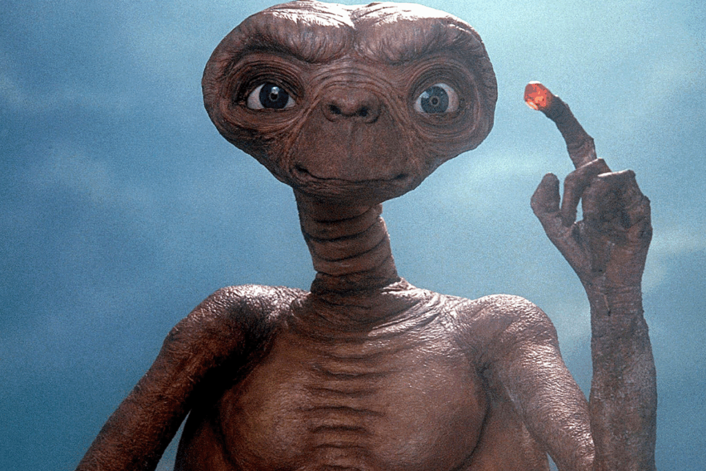E.T olhando de frente para a câmera e com o dedo indicador levantado