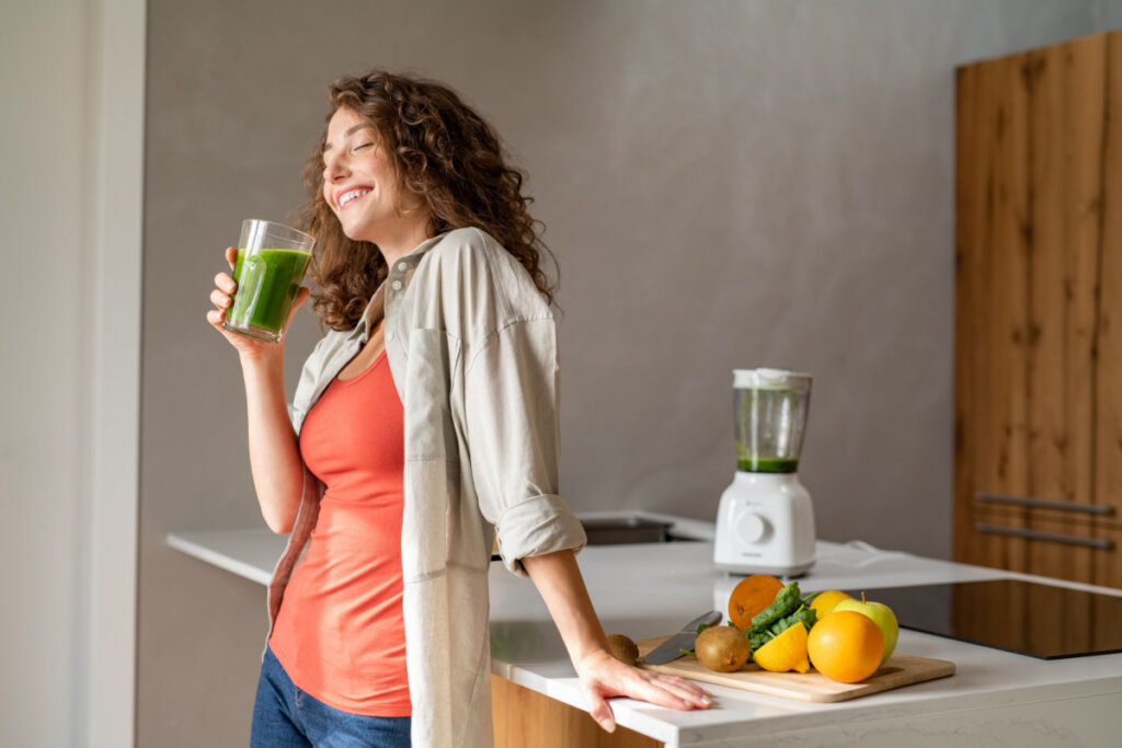 Mulher feliz bebendo suco verde em casa