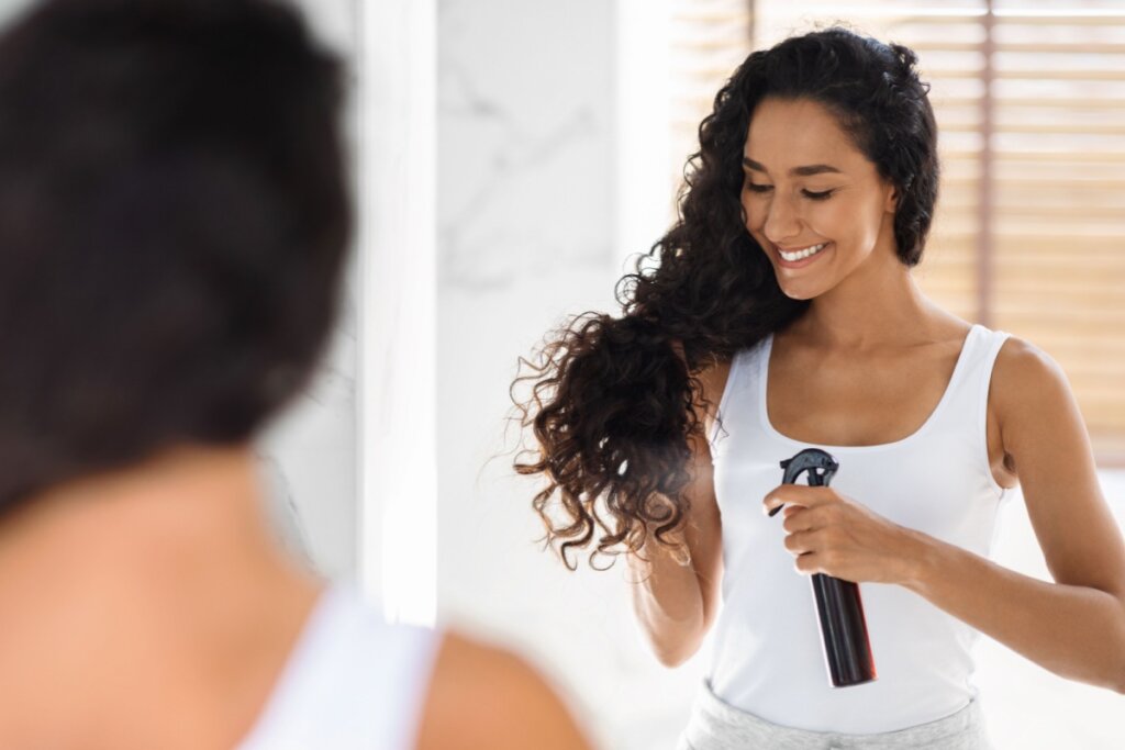 Mulher em frente a um espelho passando leave-in no cabelo 