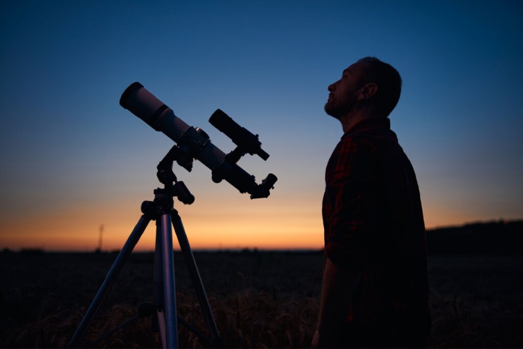 Homem em frente a um telescópio ao anoitecer