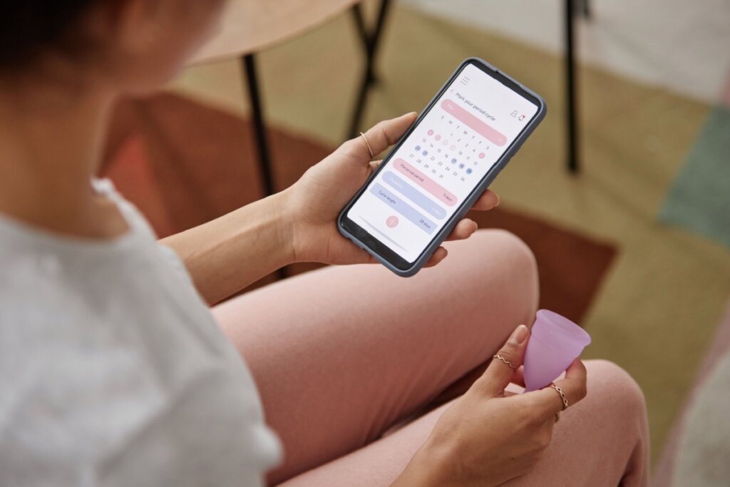 Mãos de uma mulher segurando um celular e coletor menstrual
