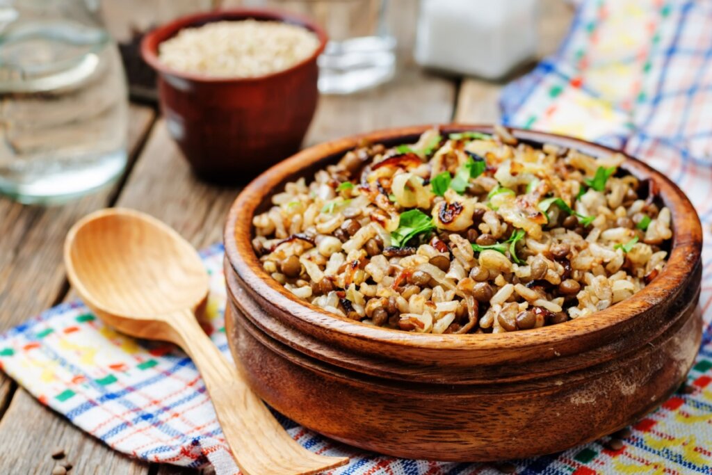 Tigela de madeira com arroz e lentilha em cima de mesa de madeira com colher de madeira ao lado