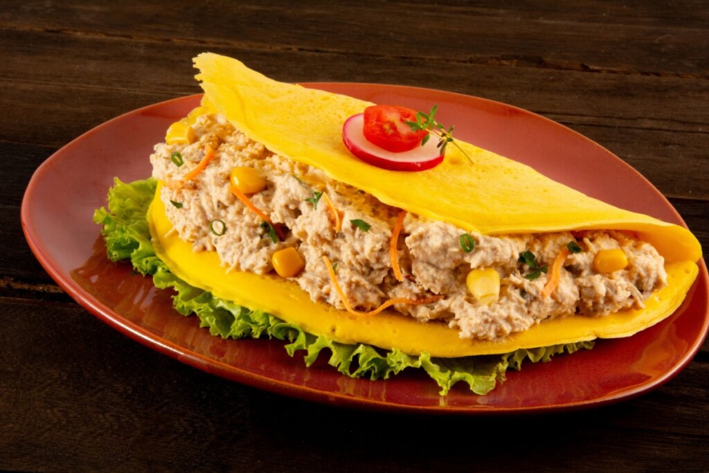 Crepioca de frango com milho servida em prato vermelho em cima de mesa de madeira