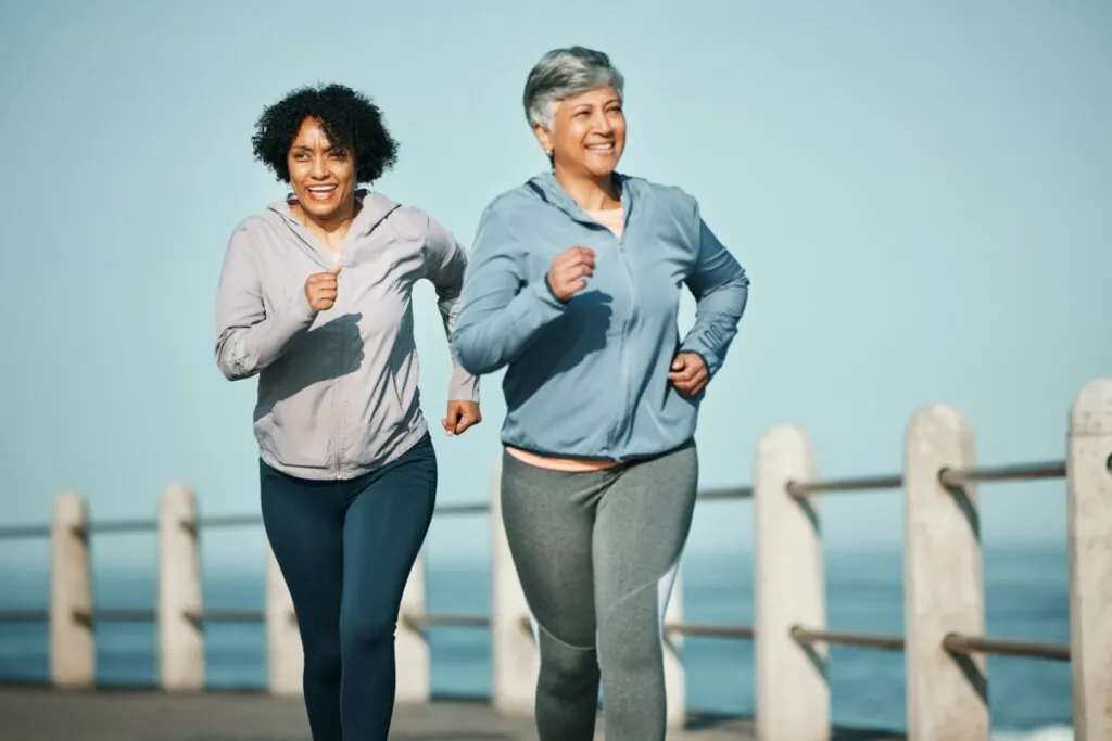 Duas senhoras com blusa de frio sorrindo e correndo em dia com céu azul