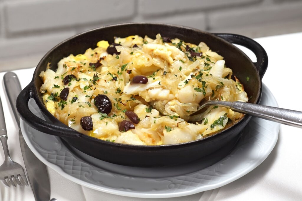 Bacalhau de forno com batatas, cebola, ovos cozidos, azeitonas pretas e salsinha picada, servido em prato fundo preto