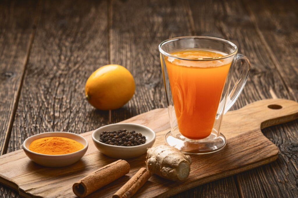 Chá termogênico em caneca de vidro ao lado de gengibre, canela, cúrcuma, pimenta-preta e laranja sobre tábua de madeira