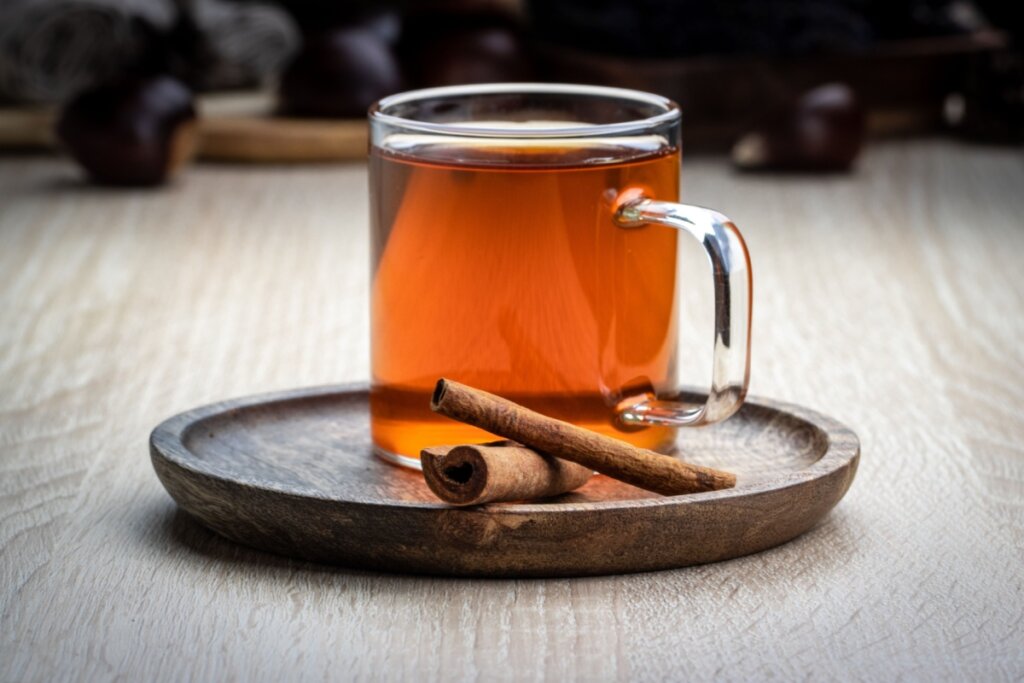 Chá de espinheira-santa com canela em caneca de vidro e em cima de um recipiente de madeira 