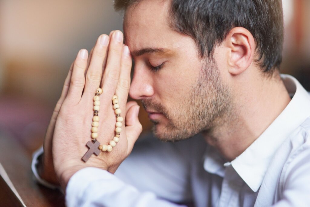 homem rezando com as mãos juntas e com terço próximo ao rosto