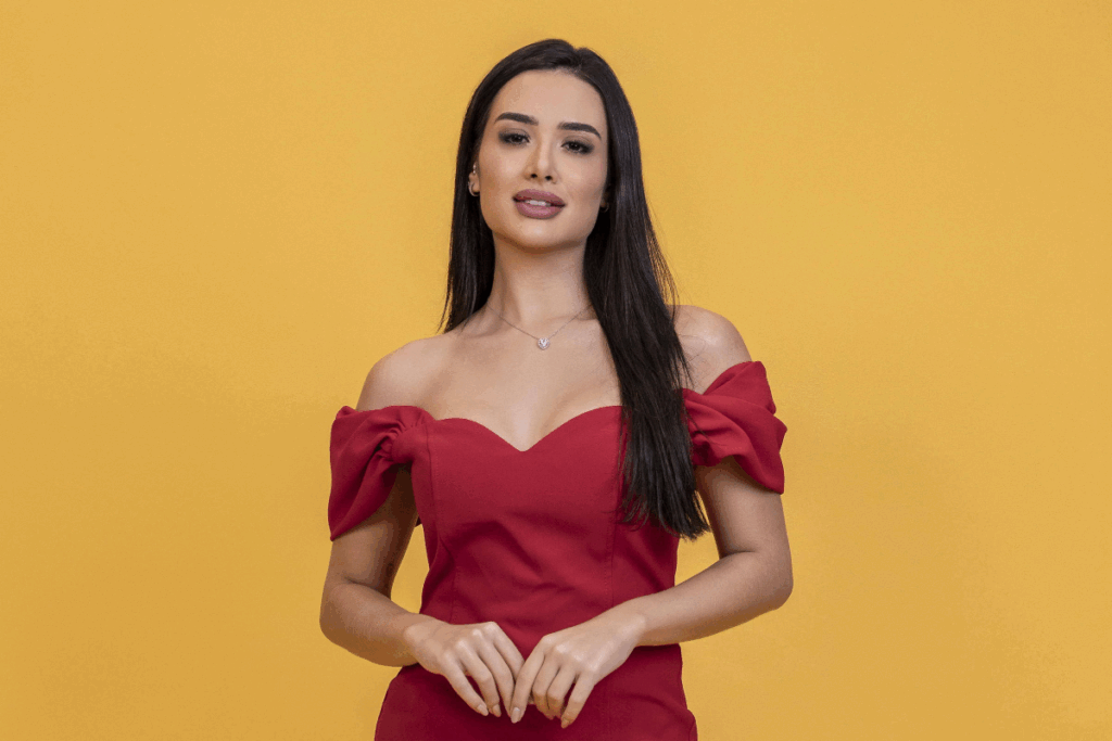 Mulher com o cabelo longo, liso e preto, usando blusa vermelha sem alça em fundo laranja