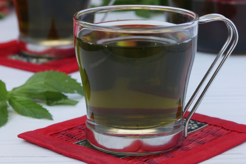 Xícara de vidro com chá de matcha com capim-limão em cima de um pano vermelho 