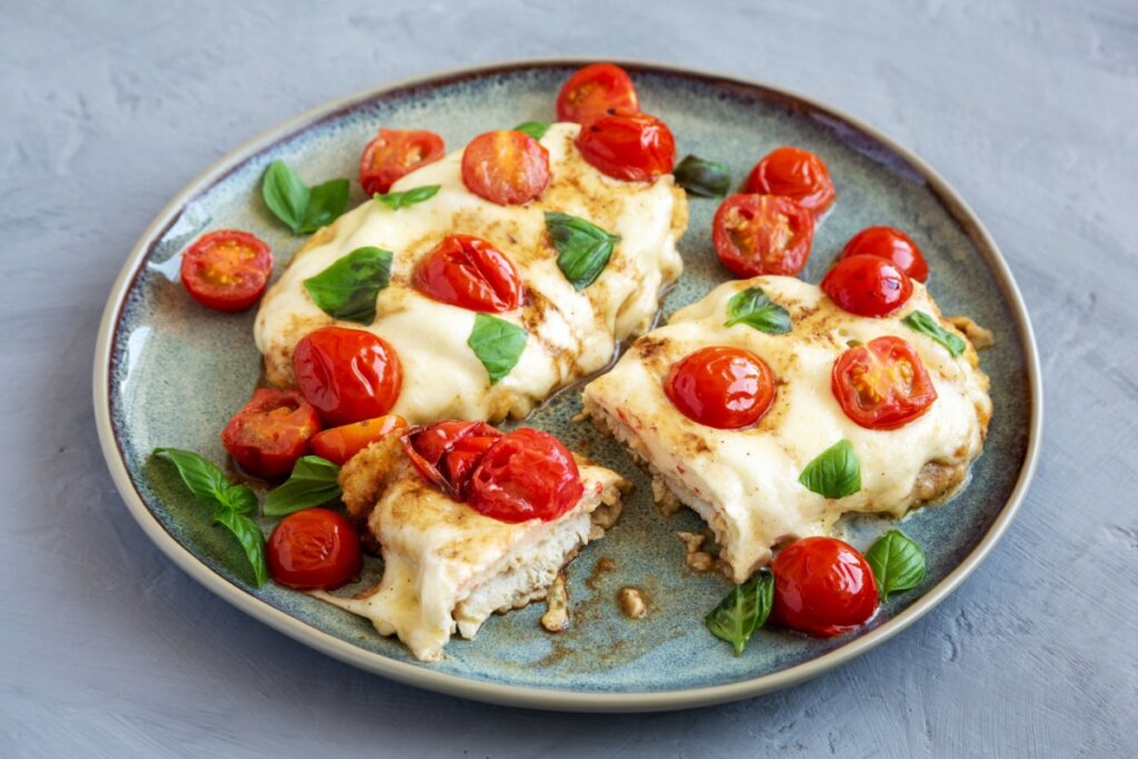 Três pedaços de frango caprese em um prato verde com tomate-cereja