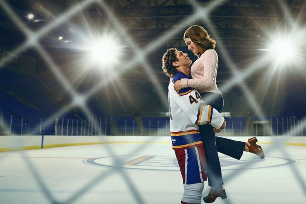Cena da série " Off Campus" com um homem usando roupa de hóquei e segurando uma mulher no colo em uma pista de hóquei 