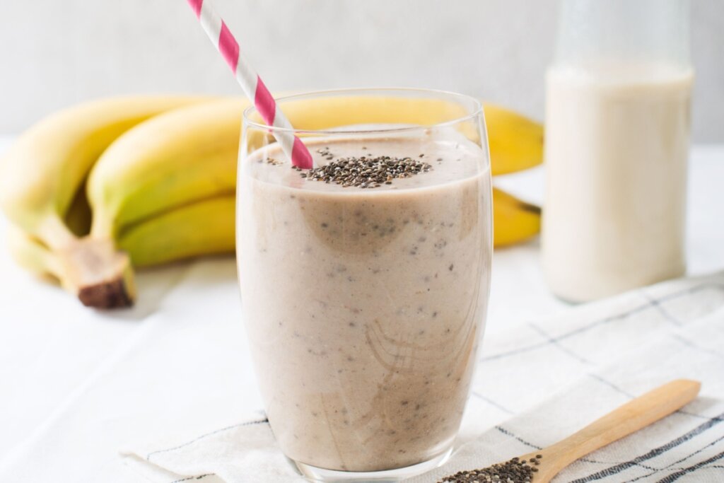 Copo de vidro com smoothie de banana com chia e um canudo vermelho e branco 