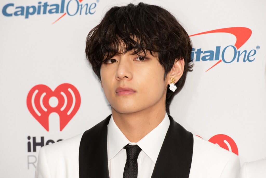 Homem com cabelo preto e franja, usando terno branco com detalhes em preto e gravata preta
