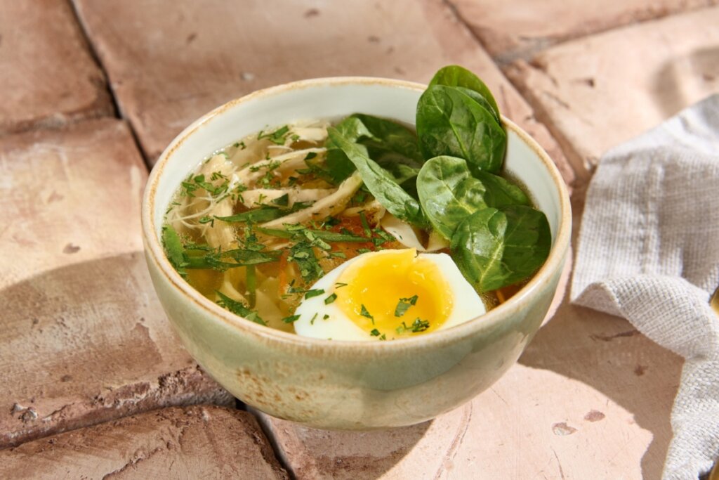 Recipiente com sopa de espinafre com frango e ovo em uma mesa de madeira