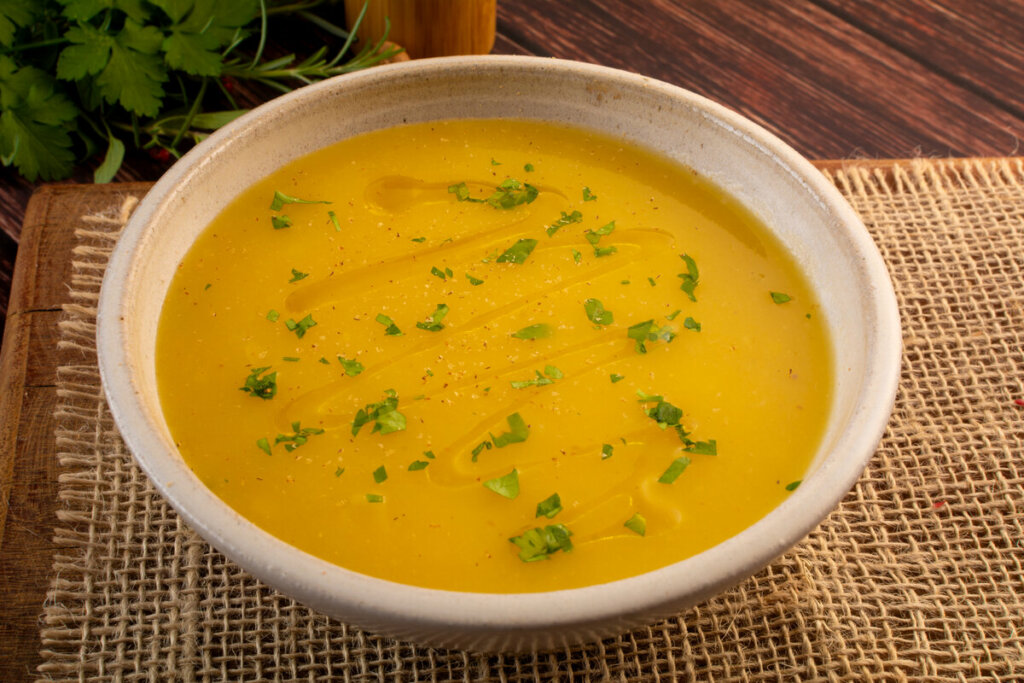 Recipiente branco com sopa amarela polvilhada com coentro