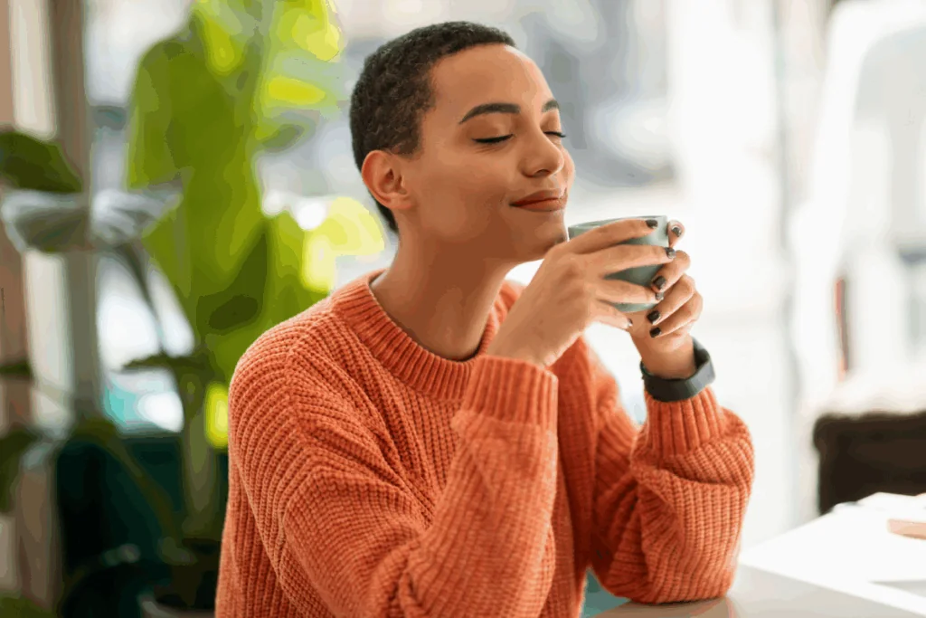Mulher com o cabelo curto, usando suéter de lã laranja, tomando chá em caneca