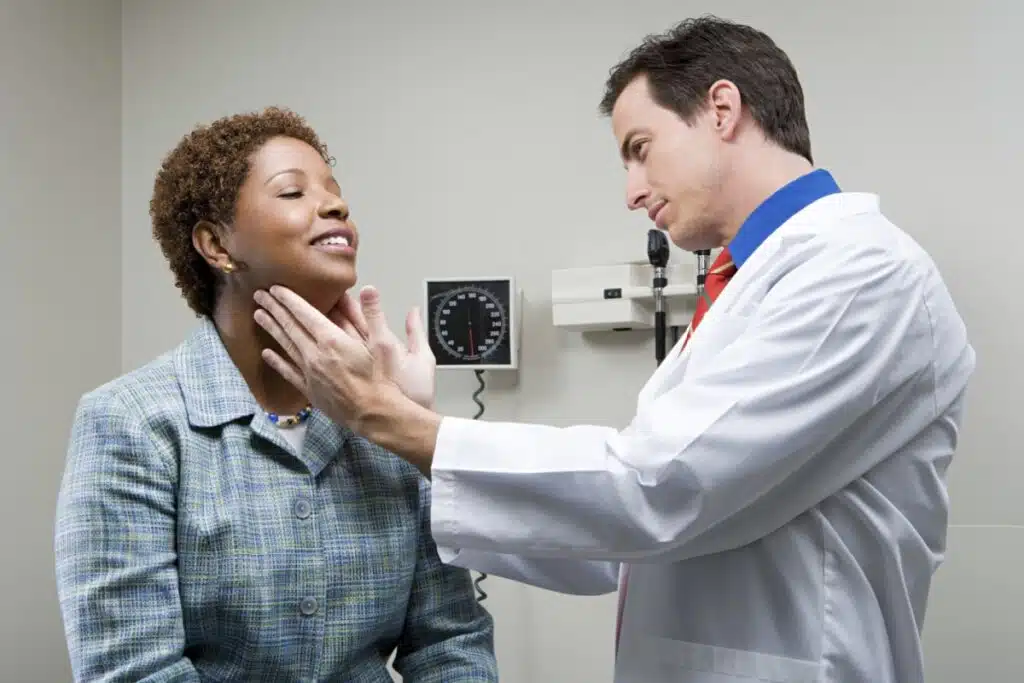 médico de jaleco branco com as mãos em pescoço de pacientes, que está sentada com a cabeça levantada