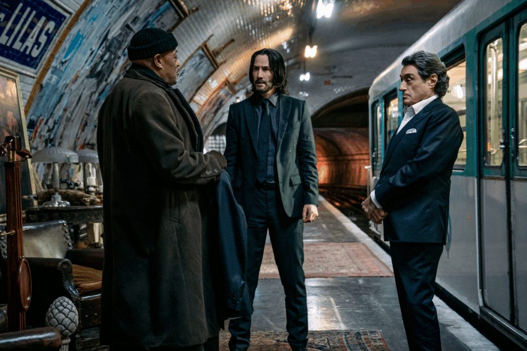 Três personagens em pé conversam em um metrô em cena de "John Wick 4: Baba Yaga"