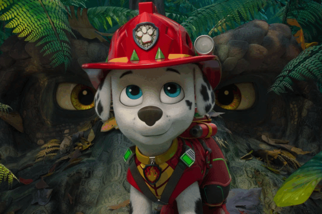 Animação em 3D do filhote dálmata Marshall, vestindo seu capacete e uniforme vermelho de bombeiro, olhado para a frente em uma floresta tropical. Ao fundo, entre a vegetação, aparecem dois grandes olhos amarelos de um dinossauro observando-o.