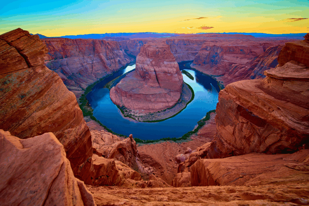 Curva do rio Colorado em formato de ferradura (Horseshoe Bend) cercada por altos paredões de rocha arenito sob um céu com tons de pôr do sol.