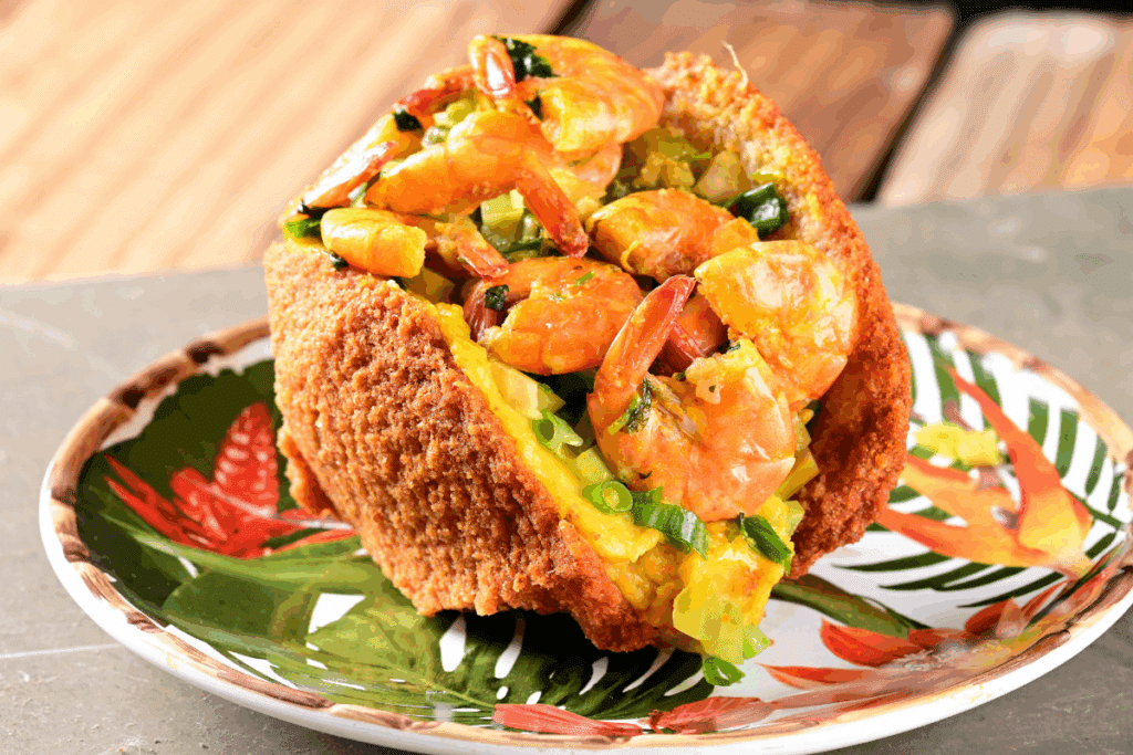 Acarajé com vatapá, camarrão e cebolinha em prato branco com estampa de plantas